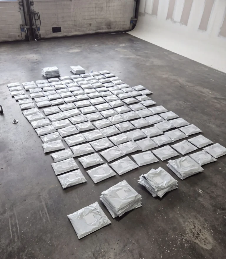 Une centaine de colis blancs alignés en rangées sur le sol en béton d'un local, prêts à être expédiés.
