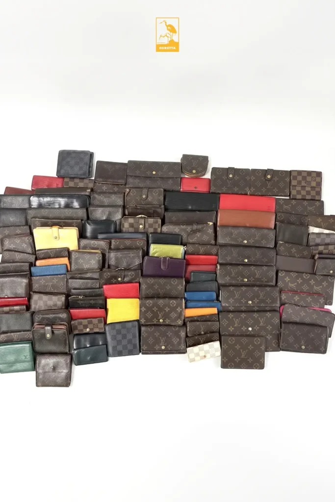 Lot d'une centaine de portefeuilles Louis Vuitton de seconde main, en toile Monogram, damier et cuir de couleur, disposés à plat sur fond blanc sous le logo EGRETTA.