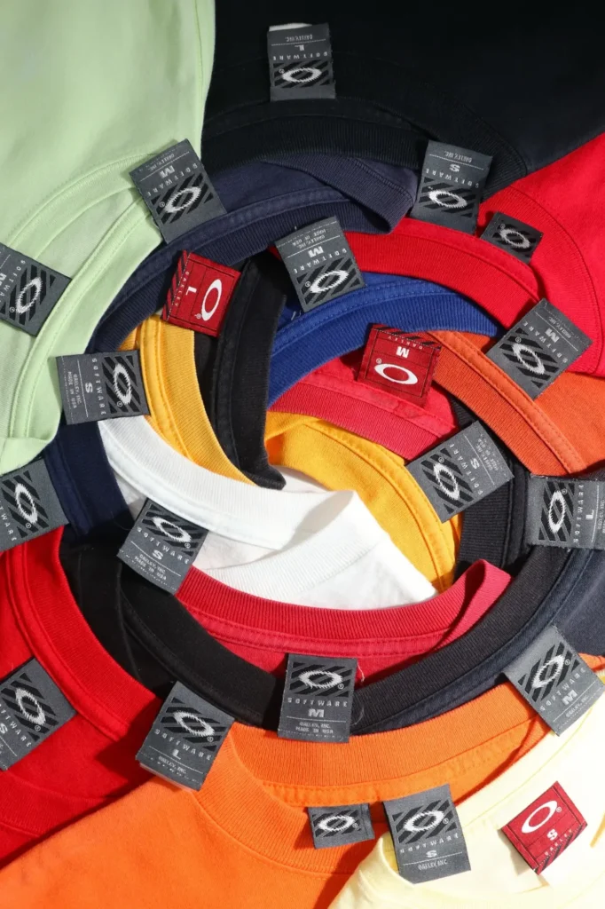 T-shirts vintage Oakley de couleurs vives disposés en spirale, cols et étiquettes apparents.